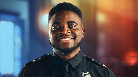 A smiling police officer in uniform with a badge looks confidently at the camera