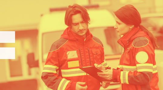 A man and woman in red jackets standing next to an ambulance, ready to provide medical assistance.