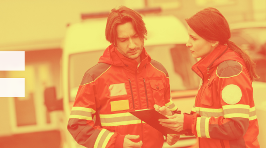 A man and woman in red jackets standing next to an ambulance.