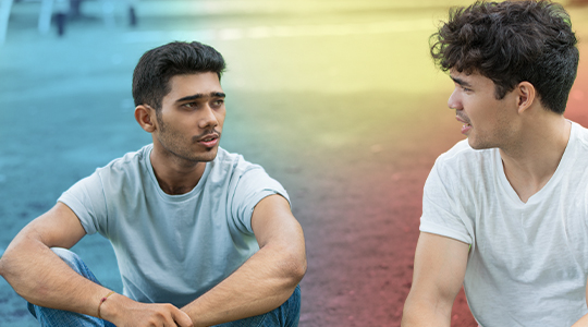 Two young men sit outdoors and have a serious conversation, facing each other attentively