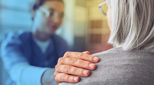 A healthcare provider places a reassuring hand on the shoulder of an older patient during a consultation, conveying compassion and support
