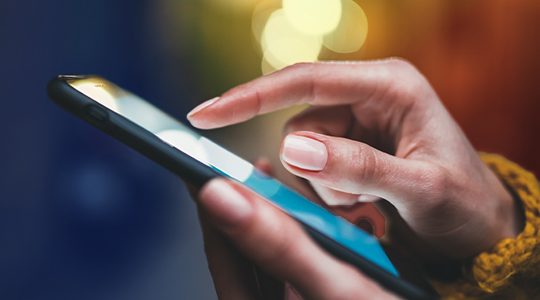A close-up of a person's hand tapping on a smartphone screen with a bokeh-lit background"