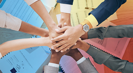 A diverse group of colleagues stacking their hands together in a show of teamwork and unity in a workplace setting